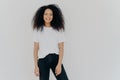 Photo of smiling woman with curly dark hair, has slim figure, wears white t shirt and black jeans, has glad face expression, Royalty Free Stock Photo