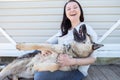 Photo of smiling woman in jeans and white jacket sitting next to happy shepherd puppy against white wooden building