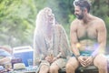 Smiling young blond woman and shirtless bearded man sitting with drinks on pier