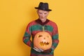 Photo of spooky man on halloween party, wearing stripes old sweater and black hat, creepy guy holding carved pumpkin isolated over Royalty Free Stock Photo