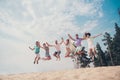 Photo of sportive carefree inspired friends hold hands jump wear casual outfit nature summer seaside beach