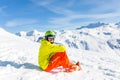 Photo of sportive man wearing helmet wearing yellow jacket sitting on snowy slope Royalty Free Stock Photo