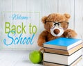 Photo of a stack of books with a bear, an apple and a place for an inscription on a wooden background. Back to school concept.