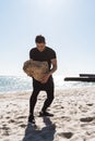 Photo of strong brunette man walking along beach by seaside and carrying big stone in his hands Royalty Free Stock Photo