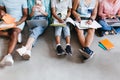 Photo of studying students writing lecture in their textbooks while sitting on the floor. Indoor portrait of university