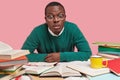 Photo of stupefied dark skinned man stares with widely opened eyes, dressed in green sweater, surrounded with much