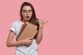 Photo of stupefied European woman has shocked facial expression, bated breath, carries spiral notepads, points with