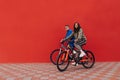 Photo of stylish man and woman riding a bicycle on the street on a background of a red wall. Stylish sports couple of cyclists