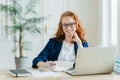 Photo of successful ginger female freelancer has remote work, watches webinar online on laptop computer, writes down information