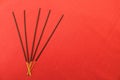 Black incense sticks with yellow tips lie in a fan on the left on a red textile background.