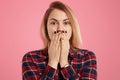Photo of surprised attractive blonde woman has black manicure, covers mouth with surprisement, dressed in stylish checkered shirt