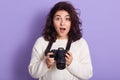 Photo of surprised beautiful cute young woman opening her mouth and eyes widely, holding her camera in both hands, having shocked Royalty Free Stock Photo