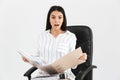 Photo of surprised brunette businesswoman 30s smiling and holding bunch of paper folders while sitting in black armchair in office Royalty Free Stock Photo