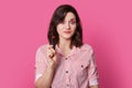 Photo of surprised brunette young woman with trendy hairstyle, has shocked expression, holds red lipstick, wears striped shirt,