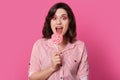 Photo of surprised European young woman with wide opened mouth, has visage, holds tasty candy , dressed in striped shirt, isolated