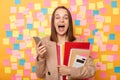 Photo of surprised happy pleased young adult woman holding paper documents and mobile phone, looking at camera screaming happily, Royalty Free Stock Photo