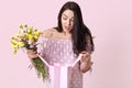 Photo of surprised terrified young woman has stupefied facial expression while opens gift bag, holds bouquet of flowers, wears