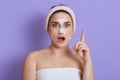 Photo of surprised woman with facial mask on nose and forehead, has beauty procedures, shocked expression, points up with index