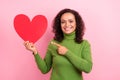 Photo of sweet charming african lady dressed green turtleneck smiling pointing finger large paper heart isolated pink