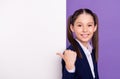 Photo of sweet charming school girl wear blue uniform pointing thumb white billboard empty space isolated purple color