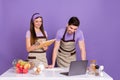 Photo of sweet cheerful boyfriend girlfriend dressed chef outfits learning new recipes gadget isolated purple color Royalty Free Stock Photo