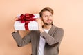 Photo of sweet funky young gentleman dressed blazer trying guess what inside big present box isolated beige color Royalty Free Stock Photo