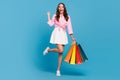 Photo of sweet lucky young woman dressed white skirt smiling rising fist holding bargains isolated blue color background