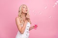 Photo of sweet pretty young lady wear white overall blowing soap bubbles pink color background