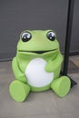 A cute lovely adorable replica statue of a bright lime luminous green frog sitting on a concrete floor