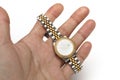 A hand holding a silver and gold ladies watch with a round watch face and diamonds on the rim