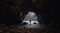 A photo taken from inside of a cave, of a man standing in front of the entrance to the cave Royalty Free Stock Photo