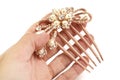A left hand holding a brown colored hairpin comb with floral design inlaid with artificial pearls and diamonds