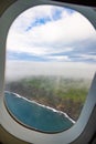 Photo taken out the window of plane, view over island with ocean and clouds Royalty Free Stock Photo
