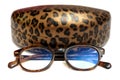 A pair of brown framed glasses with matching leopard spots print case white backdrop