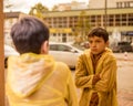 Photo of teenage boy in yellow raincoat among city streets looks into reflection of glass windows, sadness loneliness autumn Royalty Free Stock Photo