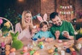 Photo of thee peaceful cheerful people hold tassel paint eggs prepare festive weekend house indoors