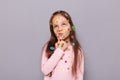 Photo of thoughtful pensive little brown haired little girl covered with stickers posing isolated over gray background, holding