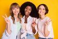 Photo of three charming cheerful girls dark skin fingers show v-sign have fun isolated on yellow color background