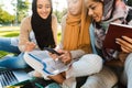 Photo of three cheerful women wearing headscarfs sitting on blanket in green park Royalty Free Stock Photo