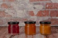 three jars of condiment sitting on a table with brick walls