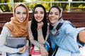 Photo of three muslim female students wearing headscarfs sitting on bench in park