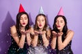 Photo of three romantic ladies blow air kiss confetti wear cone cap dresses isolated violet color background