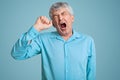 Photo of tired grey haired retired man feels sleepy, yawns as feels tired, opens mouth widely, dressed in elegant shirt, poses