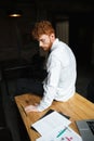 Photo of tired readhead curly bearded man, sitting on wooden tab