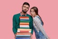 Photo of tired unshaven man with pity expression, holds pile of books, looks in displeasure, his female classmate has