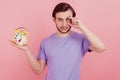 Photo of tired young man tired want sleep hold clock alarm late isolated over pastel color background
