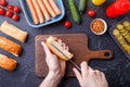 Photo on top of table with ingredients for hot dogs, cutting board, man`s hands