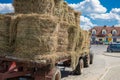 Photo of a tractor hauling hay for animal feed through the cobbled streets of a small town with houses with tiled roofs against a
