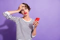 Photo of troubled upset girl hold cellphone palm brow look empty space wear striped shirt isolated purple color Royalty Free Stock Photo