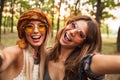 Photo of two cheerful hippie women, smiling and taking selfie while walking in forest